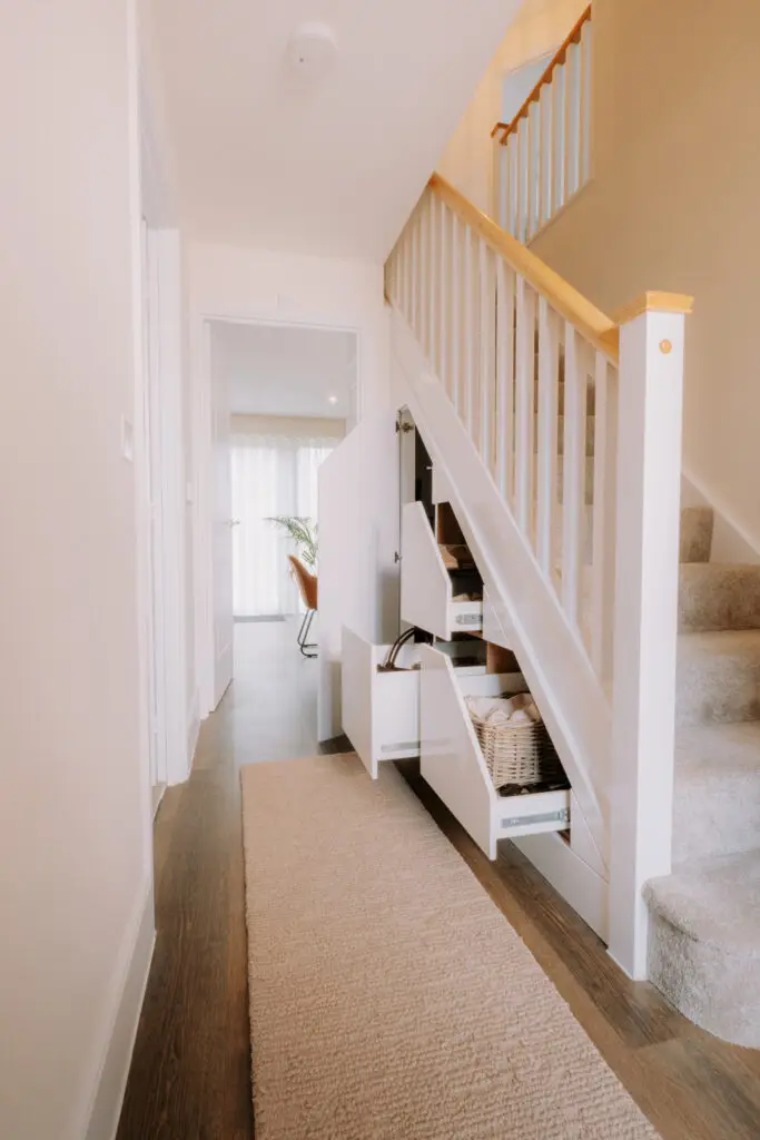 White under stairs storage unit with three pull-out drawers open in a bright modern hallway with wooden floor