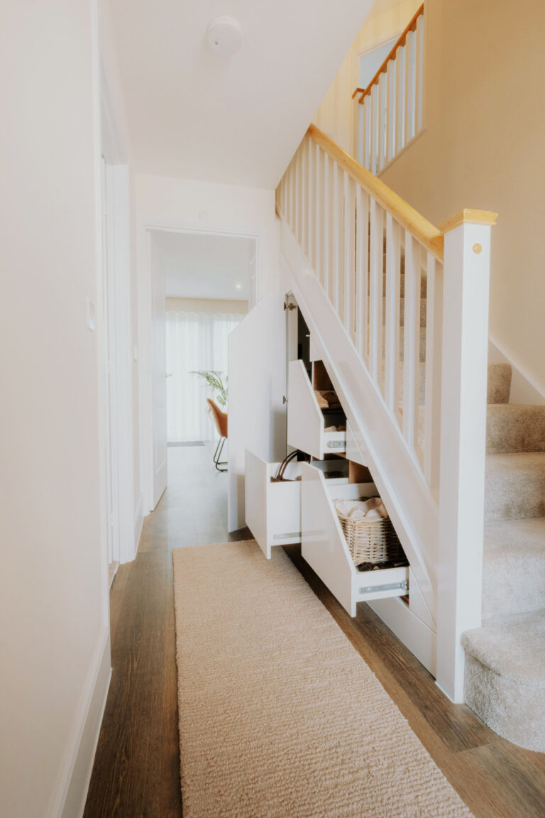 A full hallway view of fitted under-stairs storage with white drawers and a tall cupboard open.