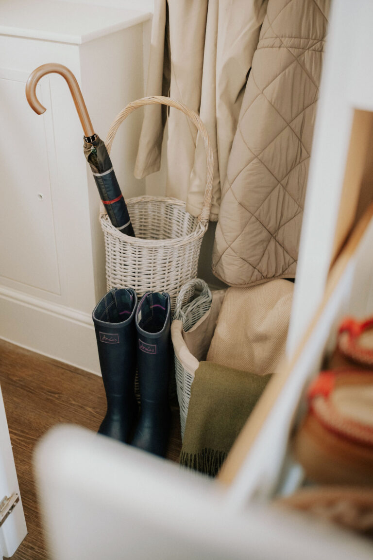 Coats, boots and an umbrella basket stored inside a tall under-stairs cupboard.
