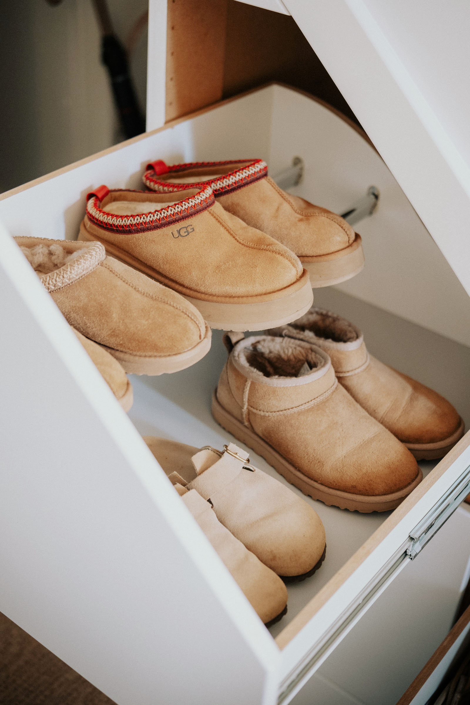Shoes and ankle boots arranged in an open white under-stairs drawer, with the drawer runner visible.