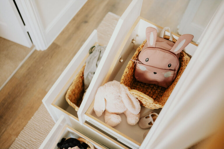 An open under-stairs drawer holding a pink children's bag, a rabbit toy and a woven basket.